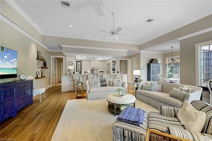 Living room featuring light wood-type flooring, wood ceiling, ornamental molding, and ceiling fan with notable chandelier