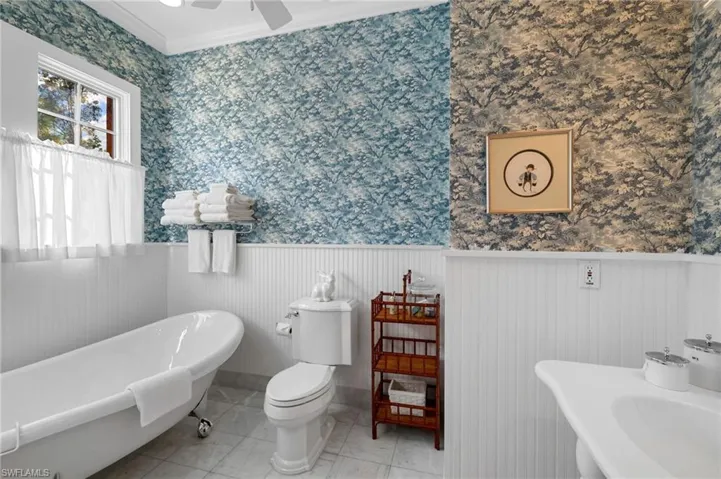 Bathroom with ornamental molding, a tub, sink, toilet, and ceiling fan
