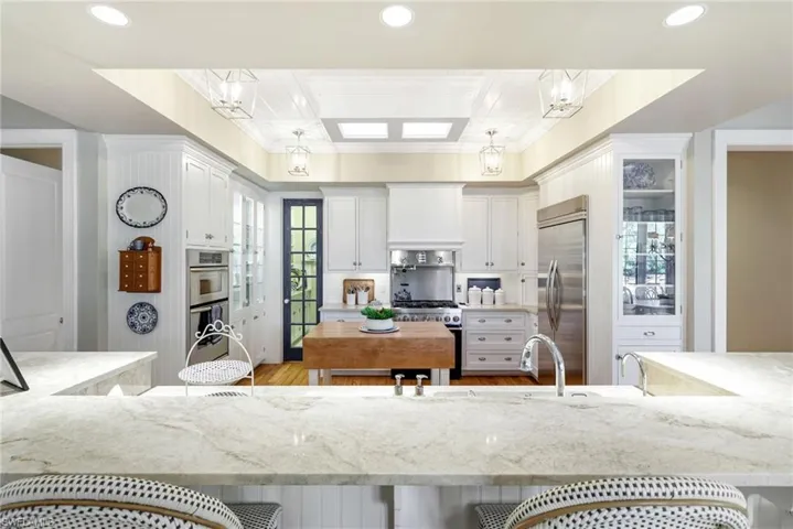 Kitchen featuring white cabinetry, a kitchen breakfast bar, high end appliances, decorative light fixtures, and light hardwood / wood-style flooring