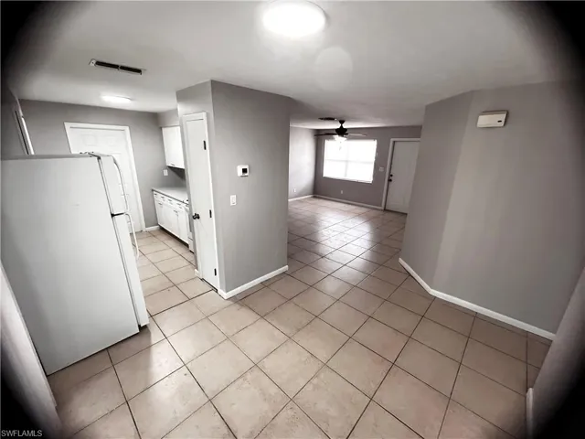 Kitchen with light tile patterned floors, freestanding refrigerator, white cabinetry, light countertops, and ceiling fan