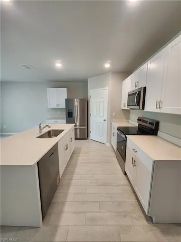 Kitchen with stainless steel appliances, white cabinets, an island with sink, recessed lighting, and light wood-type flooring