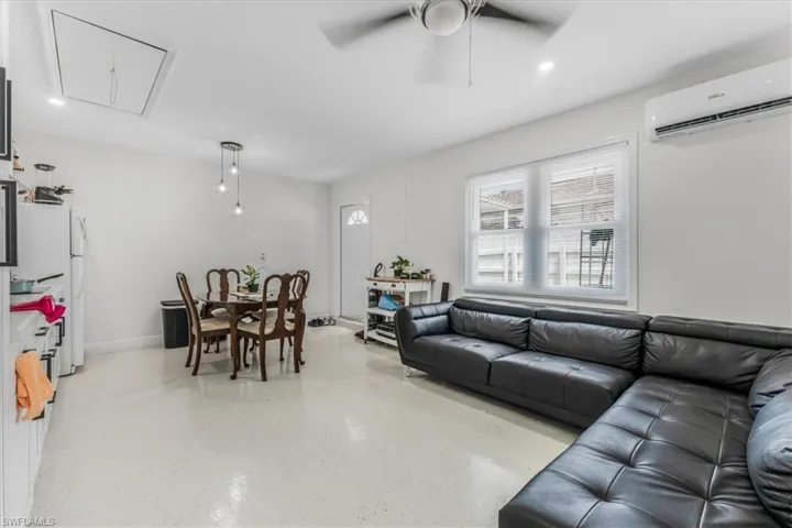 Living room with attic access, an AC wall unit, and a ceiling fan