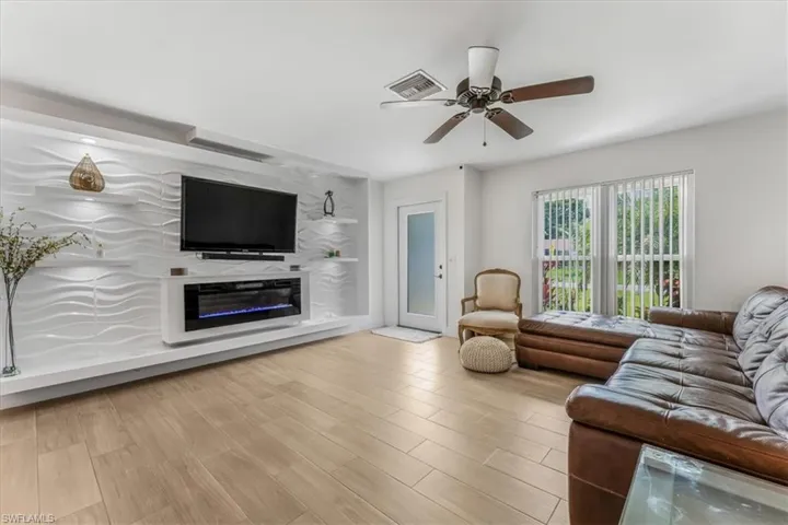 Living area featuring a ceiling fan, wood finished floors, and a glass covered fireplace