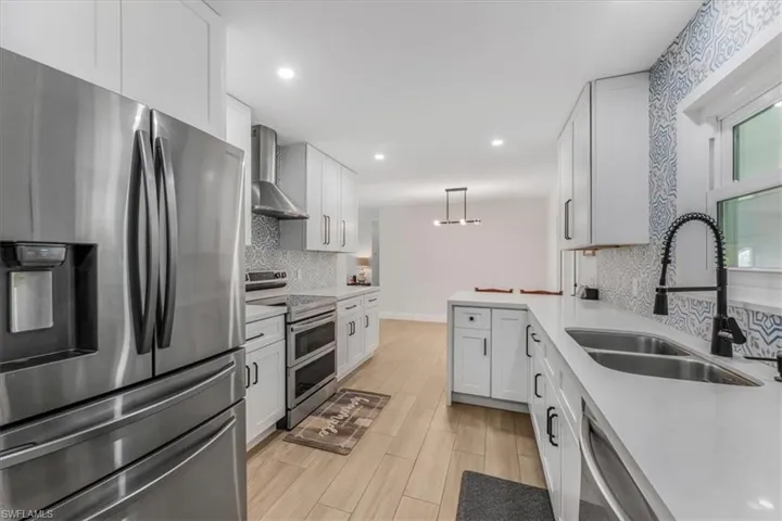 Kitchen featuring appliances with stainless steel finishes, wall chimney exhaust hood, decorative backsplash, light wood-style flooring, and light countertops