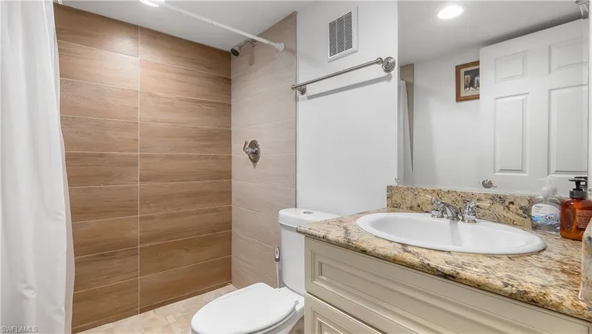Full bathroom with toilet, vanity, a shower stall, and visible vents