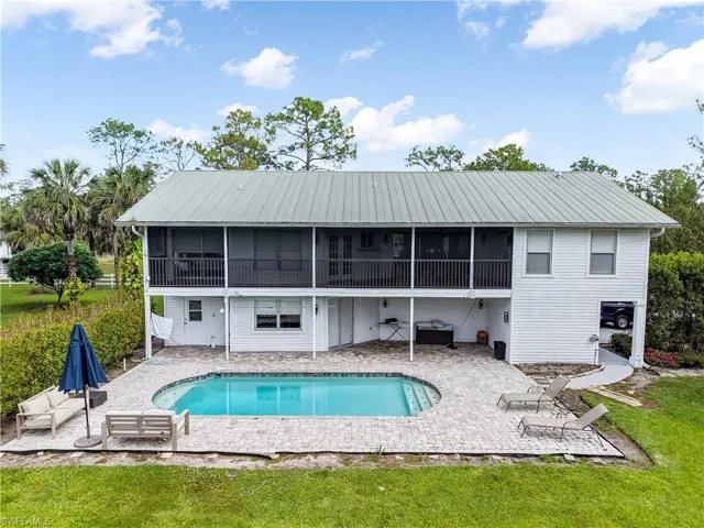 Back of property with an outdoor pool, a patio area, metal roof, a sunroom, and a lawn