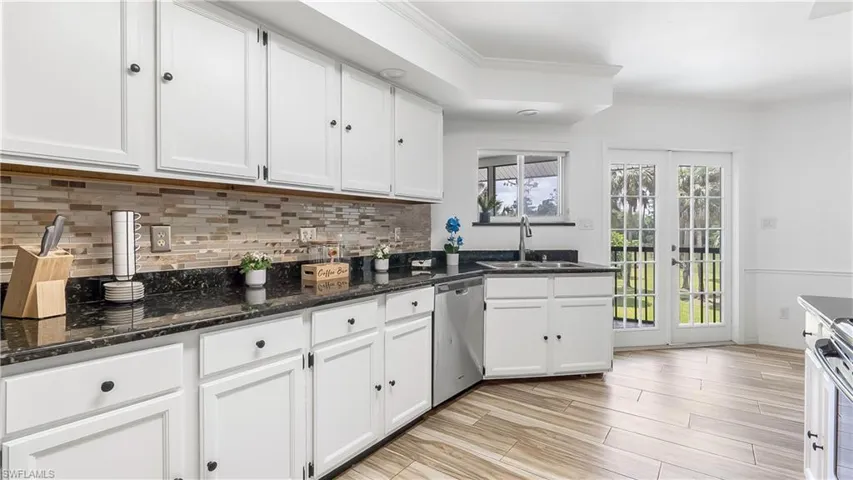 Kitchen with stainless steel dishwasher, white cabinetry, dark stone countertops, a sink, and decorative backsplash