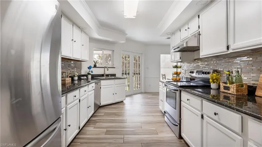 Kitchen featuring under cabinet range hood, white cabinetry, a sink, and appliances with stainless steel finishes