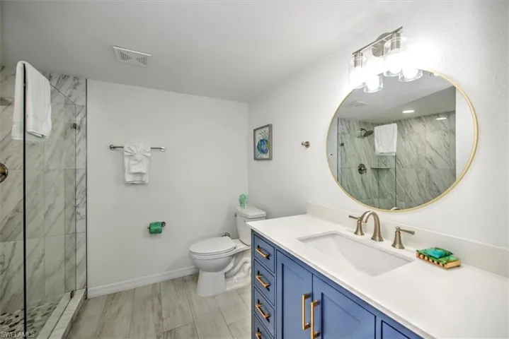 Bathroom with toilet, hardwood / wood-style floors, vanity, and tiled shower