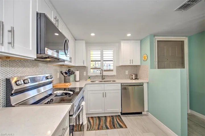 Kitchen with backsplash, stainless steel appliances, white cabinetry, and sink