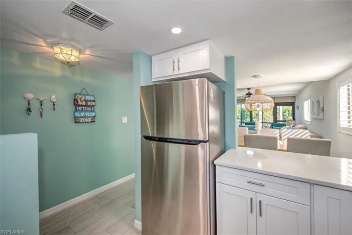 Kitchen featuring stainless steel refrigerator, white cabinetry, ceiling fan, light stone countertops, and light hardwood / wood-style flooring