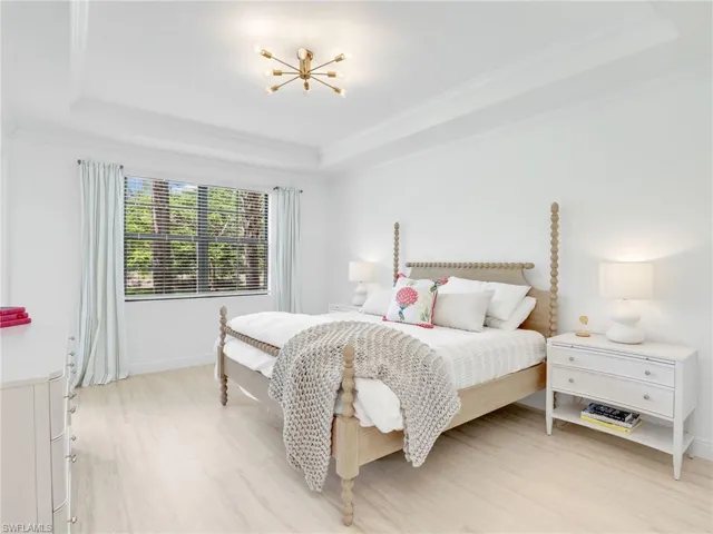 Bedroom featuring a tray ceiling, crown molding, a chandelier, and baseboards