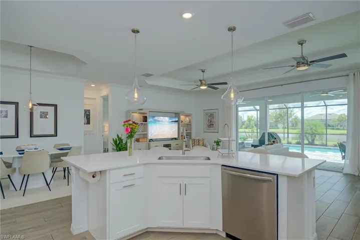 Kitchen featuring a raised ceiling, light wood finished floors, open floor plan, stainless steel dishwasher, huge quartz island and recessed lighting
