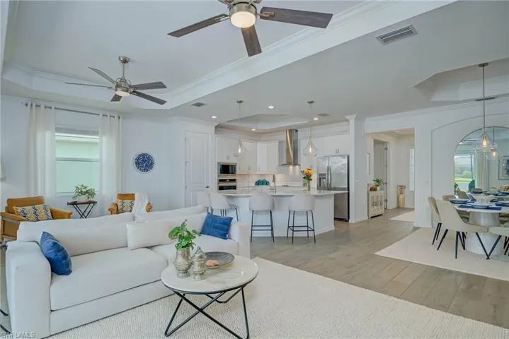 View of Great room with Chef's Kitchen, featuring a tray ceiling, light wood-style flooring, crown molding, ceiling fans, and recessed lighting