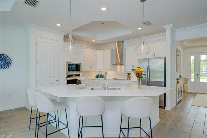 Kitchen featuring crown molding, 41" white shaker cabinetry, light wood-style flooring, stylish backsplash, and appliances with stainless steel finishes