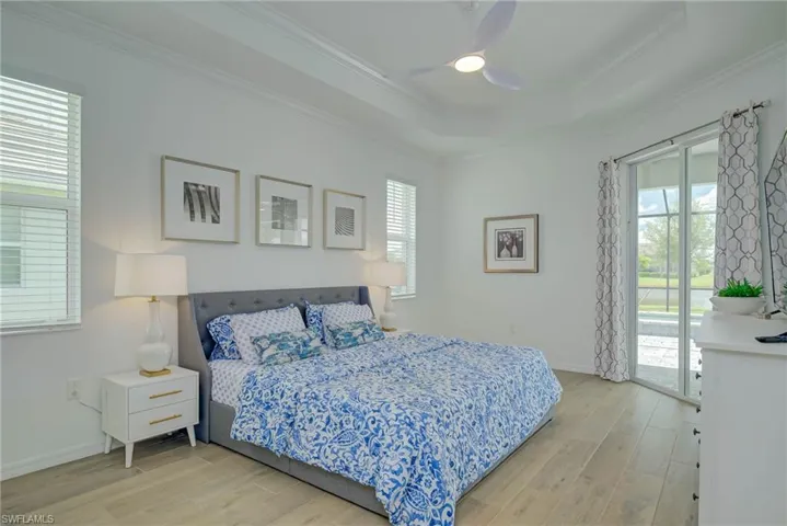 Master Bedroom with light wood-type flooring, access to lanai, a raised ceiling, crown molding, and ceiling fan