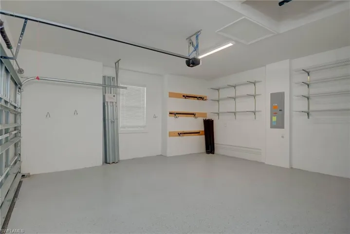 Garage with electric panel, garage door opener, epoxy flooring and wall shelving