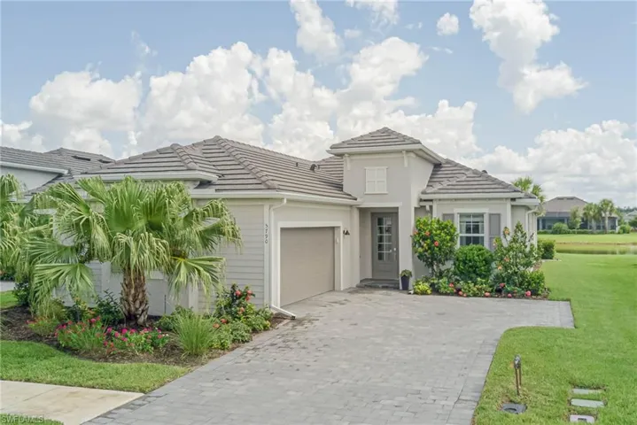 View of front of property featuring an courtyard entry style attached garage, pavers on driveway, and a tiled roof with lovely landscaping