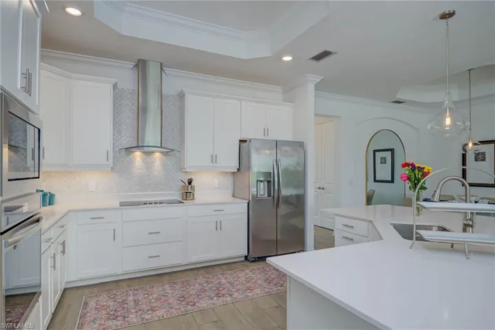 Kitchen featuring crown molding, a raised ceiling, stainless steel appliances, 42" white shaker cabinetry, and recessed lighting