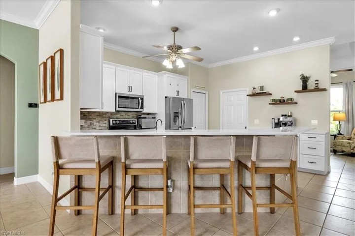 Kitchen featuring a breakfast bar, arched walkways, a peninsula, light countertops, and ornamental molding