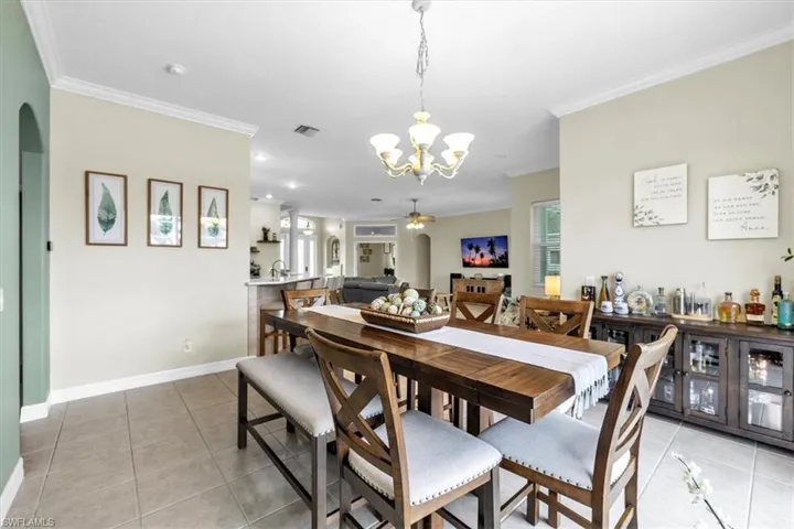 Dining space with light tile patterned flooring, ornamental molding, arched walkways, suspended lighting, and a ceiling fan