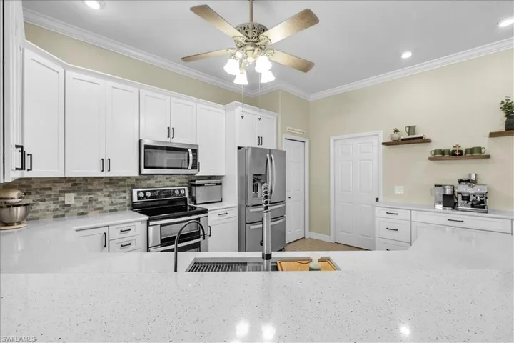 Kitchen with stainless steel appliances, white cabinetry, light stone quartz counters, a ceiling fan, and crown molding