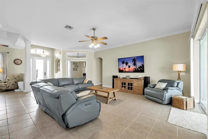 Living room featuring light tile patterned flooring, ceiling fan, arched walkways, and ornamental molding