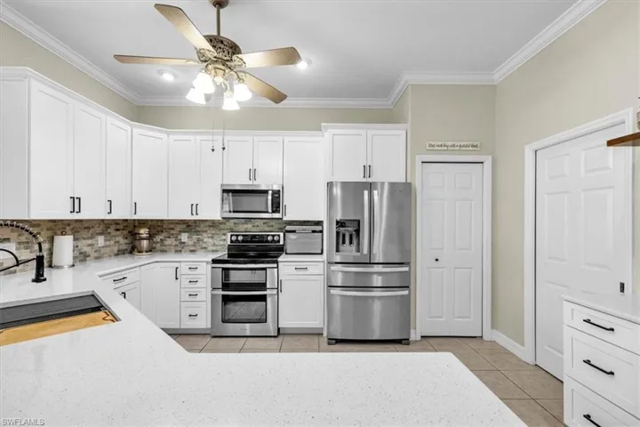 Kitchen with stainless steel appliances, light tile patterned floors, white cabinetry, light stone quartz countertops, and crown molding