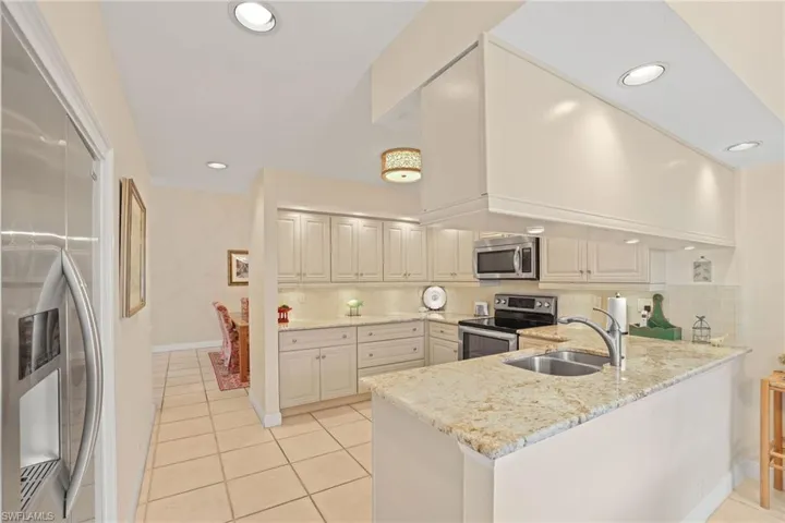 Kitchen featuring sink, stainless steel appliances, light stone counters, decorative backsplash, and kitchen peninsula