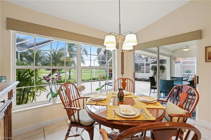 Dining room with light tile patterned floors, ceiling fan with notable chandelier, vaulted ceiling, and a healthy amount of sunlight