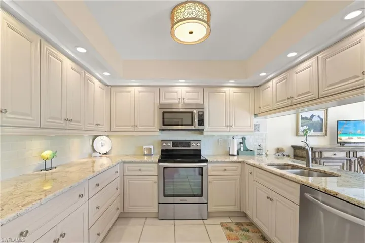 Kitchen featuring sink, light tile patterned floors, stainless steel appliances, light stone countertops, and decorative backsplash