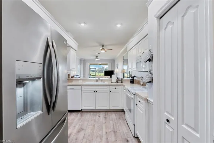 Kitchen featuring kitchen peninsula, white cabinetry, light hardwood / wood-style flooring, sink, and white appliances