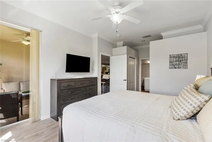 Bedroom with light hardwood / wood-style floors, ornamental molding, connected bathroom, and ceiling fan