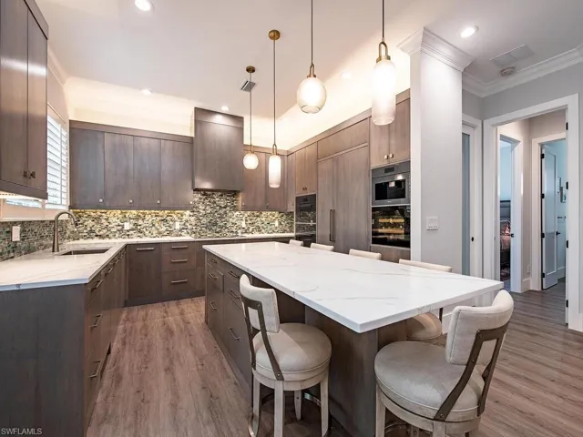 Kitchen with wood-type flooring, sink, a kitchen island, decorative light fixtures, and wall chimney exhaust hood