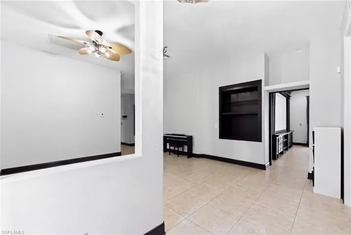Interior space featuring large-format tile flooring, built-in recessed shelving, a ceiling fan with integrated lighting, and dark-finished trim