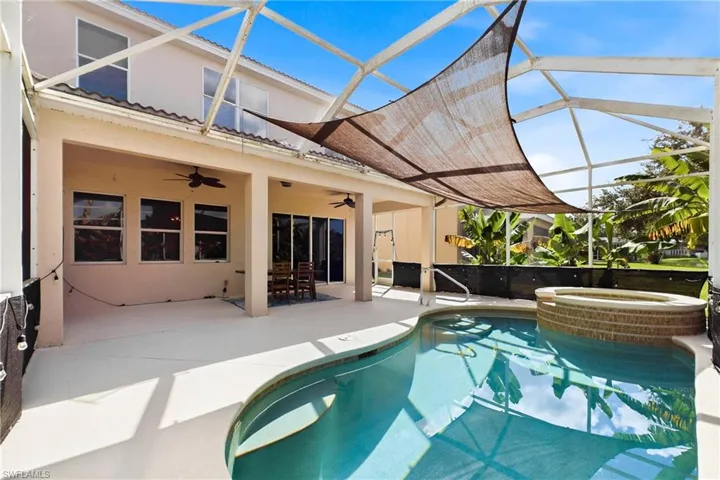 Screened-in lanai featuring a swimming pool with integrated spillover spa, expansive covered patio, dual ceiling fans, and concrete decking