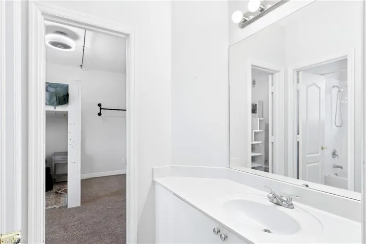 Vanity featuring an integrated sink, chrome dual-handle faucet, and an expansive wall-mounted mirror with a triple-bulb light fixture