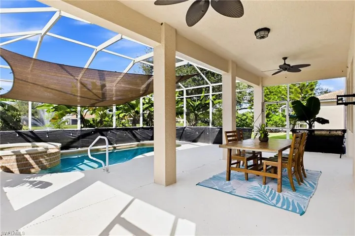 Screen-enclosed patio featuring a pool with an integrated stone-finish spa, dual ceiling fans, and concrete decking