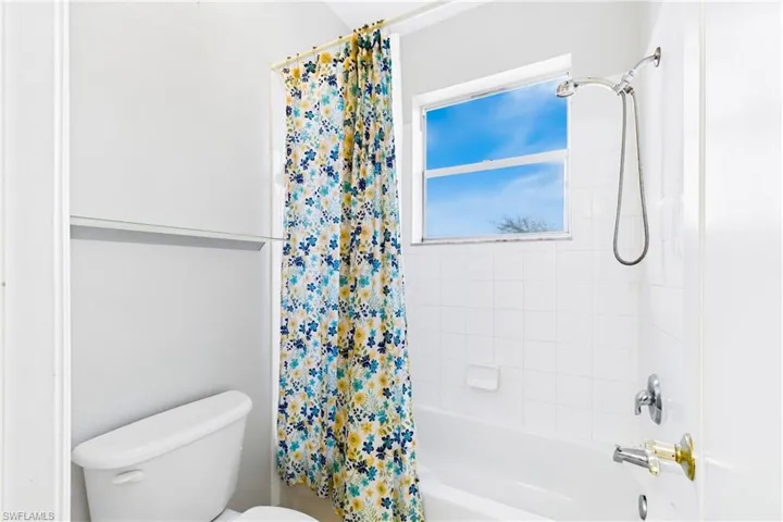 Bathroom featuring a porcelain tub, white ceramic wall tile, a window, a built-in soap dish, and a handheld shower fixture