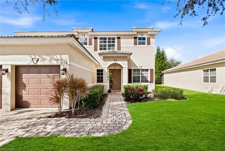 Two-story stucco exterior featuring a tiled roof, attached garage, paver walkway, and manicured landscaping