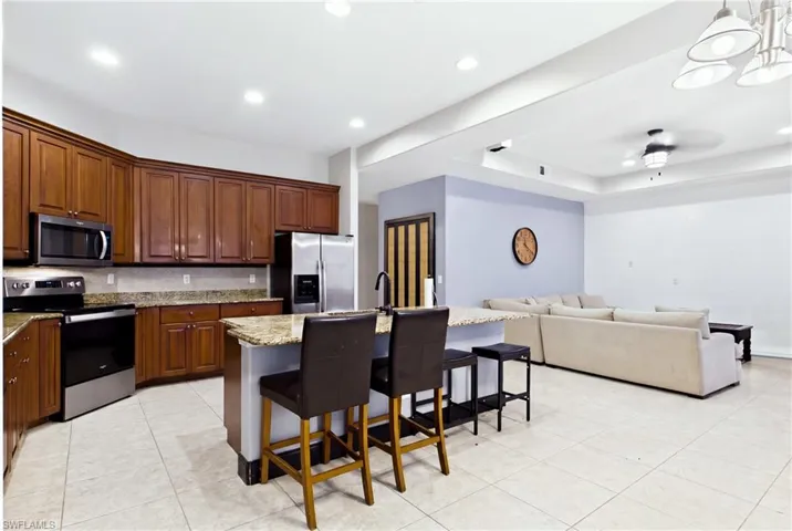 Kitchen featuring wood cabinetry, stone countertops, a center island with a high-arch faucet, stainless steel appliances, and tile flooring