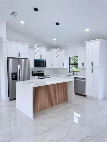 Kitchen with a center island, white cabinetry, light marble finish floors, lofted ceiling, and pendant lighting