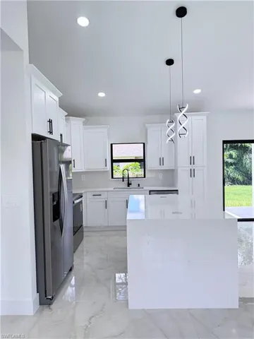 Kitchen with decorative light fixtures, light marble finish floors, stainless steel appliances, white cabinets, and recessed lighting