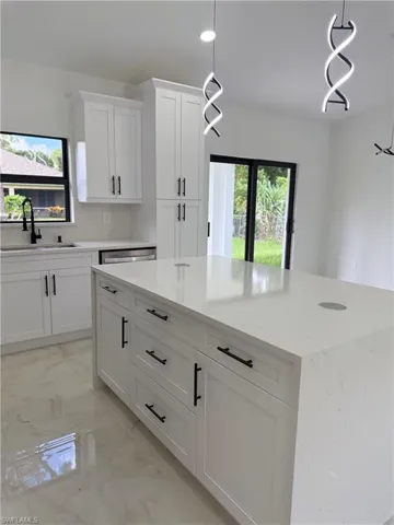 Kitchen with a center island, light marble finish floors, appliances with stainless steel finishes, hanging light fixtures, and lofted ceiling