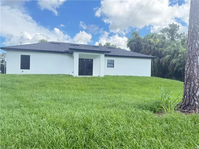 Rear view of property featuring a yard, stucco siding, and roof with shingles