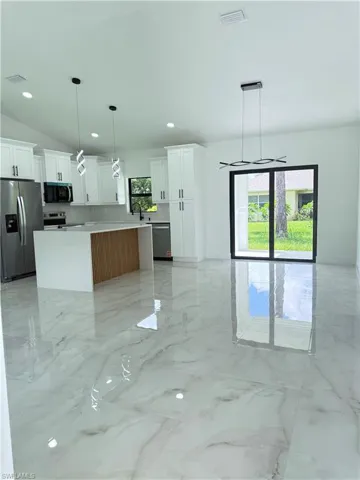 Kitchen featuring appliances with stainless steel finishes, vaulted ceiling, a kitchen island, light marble finish floors, and light stone counters