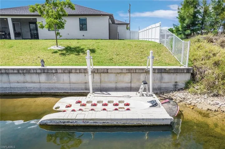 Back of property featuring stucco siding, a water view, roof with shingles, and a boat ramp