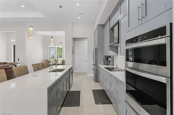 Kitchen featuring stainless steel appliances, gray cabinetry, a chandelier, a large island with sink, and wall chimney range hood