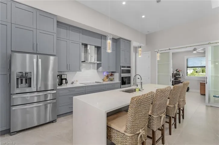 Kitchen with appliances with stainless steel finishes, gray cabinetry, wall chimney range hood, backsplash, and a kitchen bar