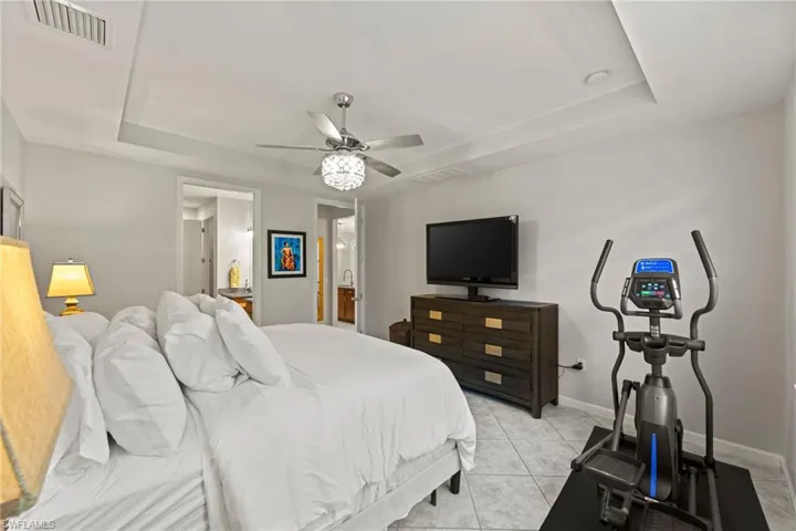 Tiled Primary en-suite bedroom featuring a tray ceiling, connected bathroom, and ceiling fan